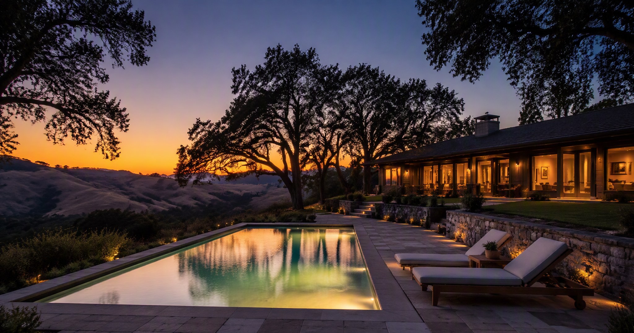 Looking down the length of a still in-ground pool at dusk with glowing underwater lights